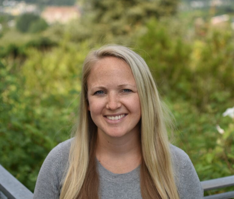 a person with long blonde hair is wearing a grey shirt and smiling at the camera