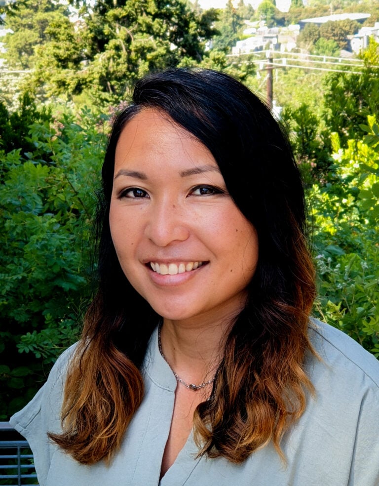 an Asian woman's headshot in front of a green forest background