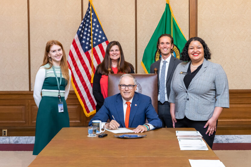 Gov. Inslee, a WSOS employee, Rep. Reed, & a legislative aid smiling for a photo as Inslee signs a bill into law.