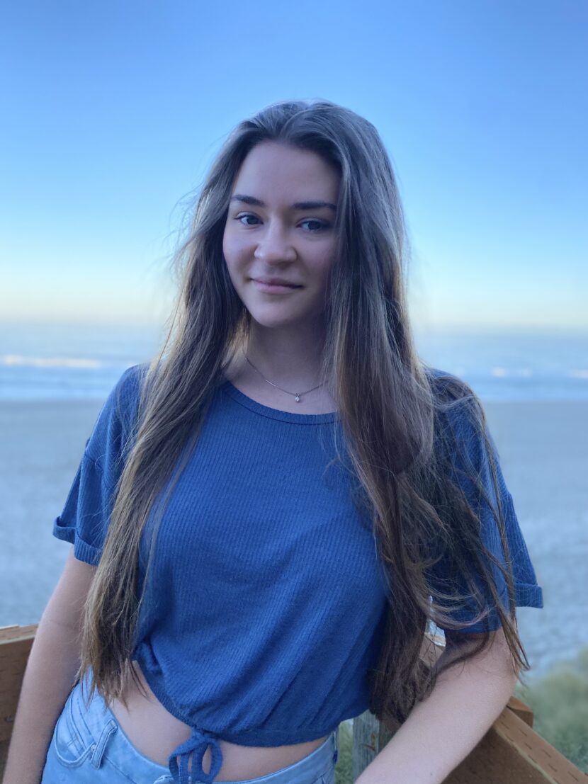 Picture of a scholar wearing a blue t-shirt with their hair down surrounded by nature in the background.