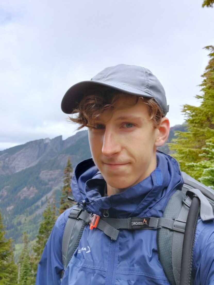 Picture of a scholar wearing hiking gears in nature with mountain in the background.  