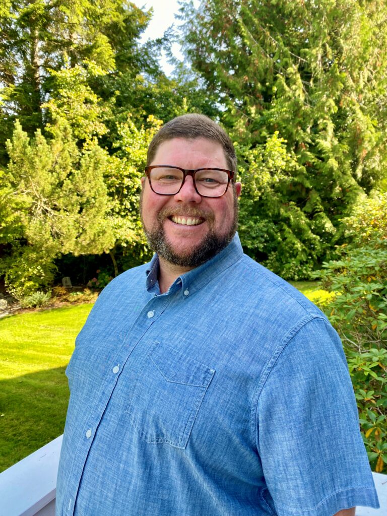 Man smiling for a photo in front of greenery