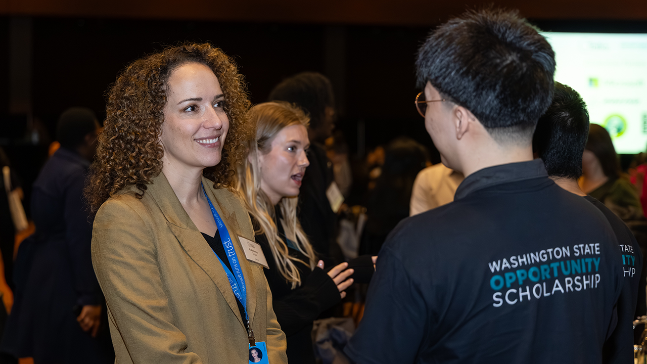 A student speaking wearing a black Washington State Opportunity Scholarship t-shirt with a corporate person wearing a tan blazer