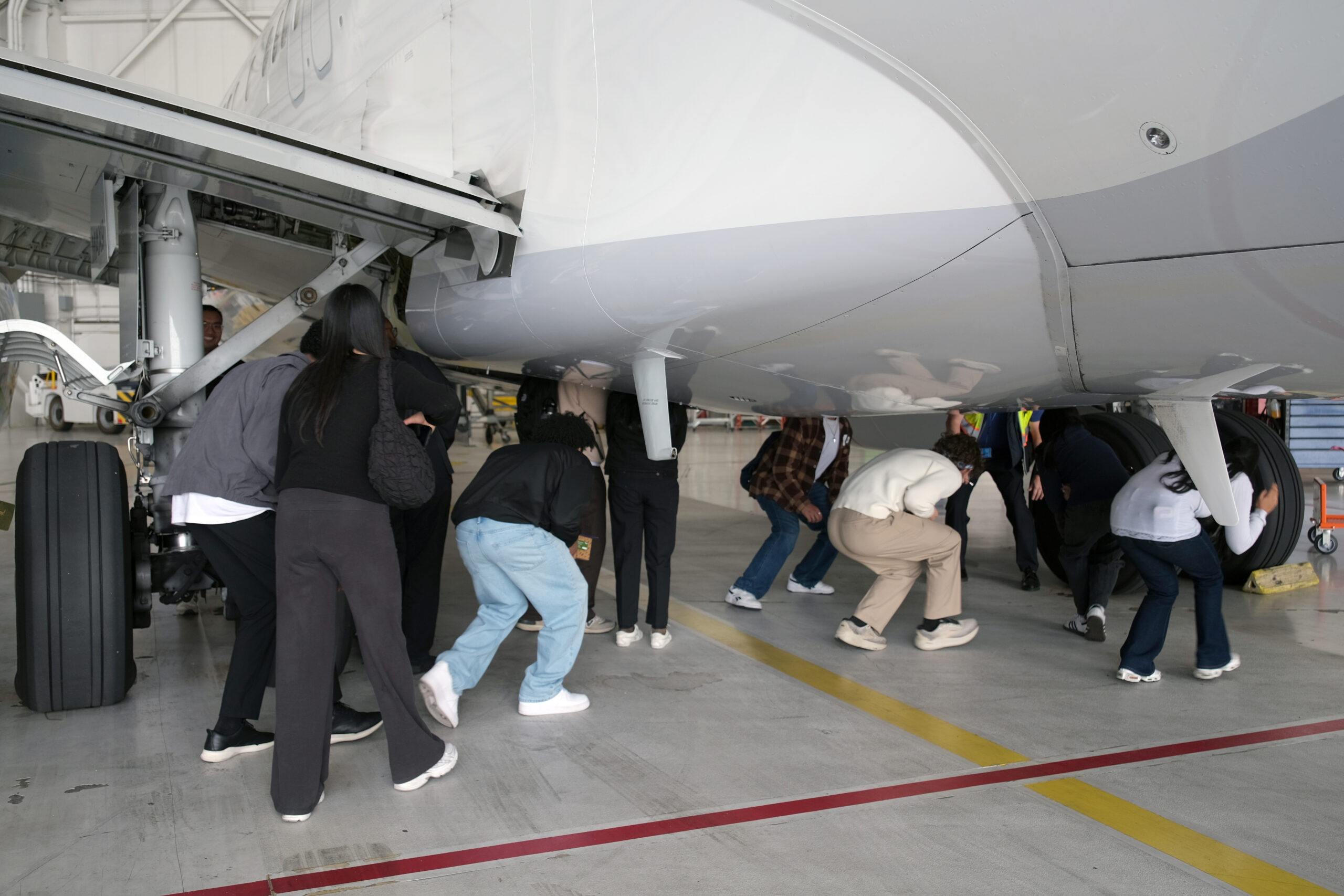 A group of Opportunity Scholars ducking under a plane in a hangar